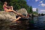 Femme assise sur le rocher avec un homme sur chambre à air dans les lacs de Belgrade, Maine, États-Unis