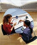 Two Businesswomen Sitting at Table with Blueprints and Datebook