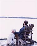 Homme assis dans la chaise Adirondack sur Dock avec chien Bala, Ontario, Canada