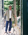 Portrait d'un homme debout dans l'embrasure de la porte avec une canne à pêche et chien Bala, Ontario, Canada