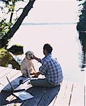 Mann sitzt auf Dock mit Hund Bala, Ontario, Kanada