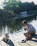 Man Sitting on Dock, Reading Newspaper with Dog, Bala, Ontario Canada