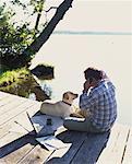 Homme assis sur le quai, à l'aide de téléphone portable avec chien, Bala (Ontario), Canada