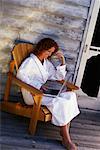 Femme en peignoir, assis dans une chaise sur le porche à l'aide d'ordinateur portable