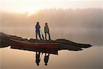 Couple Standing on Rocks in Lake With Canoe, Haliburton, Ontario Canada