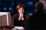 Mature Businesswoman Sitting at Desk with Mature Man