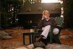 Portrait of Woman Sitting in Adirondack Chair, Using Phone Outdoors