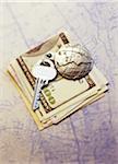 Key with Globe Keychain on Stack Of Currency on Map