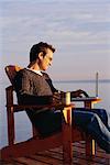 Homme assis dans une chaise sur le quai avec ordinateur portable et Mug