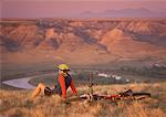 Woman Sitting in Field with Bike Overlooking Landscape, Milk River Valley, Alberta, Canada