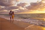 Vue arrière du Couple marchant en Surf sur la plage au coucher du soleil