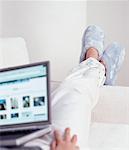 Close-Up of Woman Using Laptop Computer with Legs Hanging over Arm of Sofa