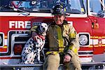 Portrait of Male Fire Fighter Sitting on Fire Engine with Dalmatian