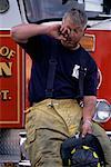 Male Firefighter Sitting on Fire Engine, Rubbing Eye