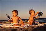 Two Babies Sitting on Beach with Pinwheels