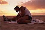 L'homme sur la plage en athlétisme porter des étirements des jambes au coucher du soleil