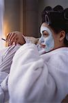 Femme en peignoir portant masque Facial avec bigoudis dans les cheveux fumer Cigarette