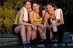 Portrait de trois jeunes femmes en vêtements d'entraînement, assis à l'extérieur portant des patins à roues alignées