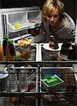 Woman Looking at Fruit Salad in Fridge with Chocolate Cake, Tofu And Juice