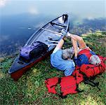 Back View of Mature Couple Relaxing on Shore with Canoe