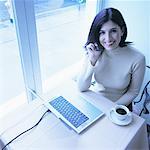 Portrait de femme assise de fenêtre en utilisant un téléphone cellulaire avec ordinateur portable sur une Table de café