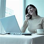 Woman Using Cell Phone at Cafe With Laptop Computer on Table