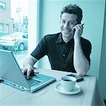 Portrait of Man Using Cell Phone In Cafe with Laptop Computer on Table