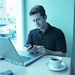 Man Using Electronic Organizer And Laptop Computer at Table in Cafe