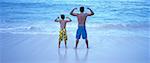 Vue arrière du père et du fils en maillot de bain, Flexing Muscles sur la plage