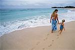 Vue postérieure de la mère et la fille en maillot de bain, marchant sur la plage main dans la main