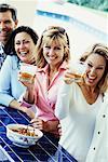 Gruppenfoto der Menschen am Tisch mit Getränken, lachend Outdoors