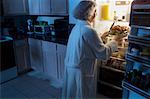 Mature femme debout au réfrigérateur ayant poulet comme collation de minuit