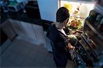 Back View of Man Standing at Fridge, Having Chicken as Midnight Snack