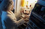 Mature femme debout au réfrigérateur après avoir gâteau comme collation de minuit