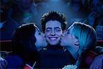Zwei junge Frauen, jungen Mann auf Wangen im Kino zu küssen