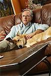 Man Sitting on Sofa with Dog Holding Remote Control