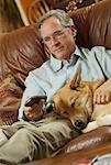 Mann sitzt auf dem Sofa mit Hund mit Fernbedienung