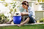 Woman Sitting on Ground and Dog Drinking from Bucket