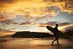 Silhouette d'homme avec planche de surf sur la plage