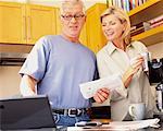 Couple Standing in Kitchen Holding Bills and Looking at Laptop
