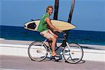 Man Riding Bike and Carrying Surfboard