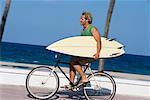 Man Riding Bike and Carrying Surfboard