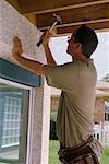 Man Hammering Exterior of House