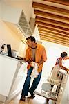 Couple in Kitchen Using Laptop Computer and Washing Dishes