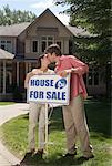 Couple Kissing by House for Sale Sign