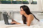 Femme allongée sur le lit avec ordinateur portable et le journal