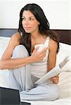 Woman Sitting on Bed with Newspaper and Laptop