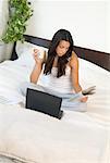 Frau sitzt auf dem Bett mit Zeitung und Laptop