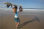 Femme en cours d'exécution sur la plage avec planche de surf