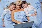 Mother and Daughters in Bed, Looking at Laptop Computer